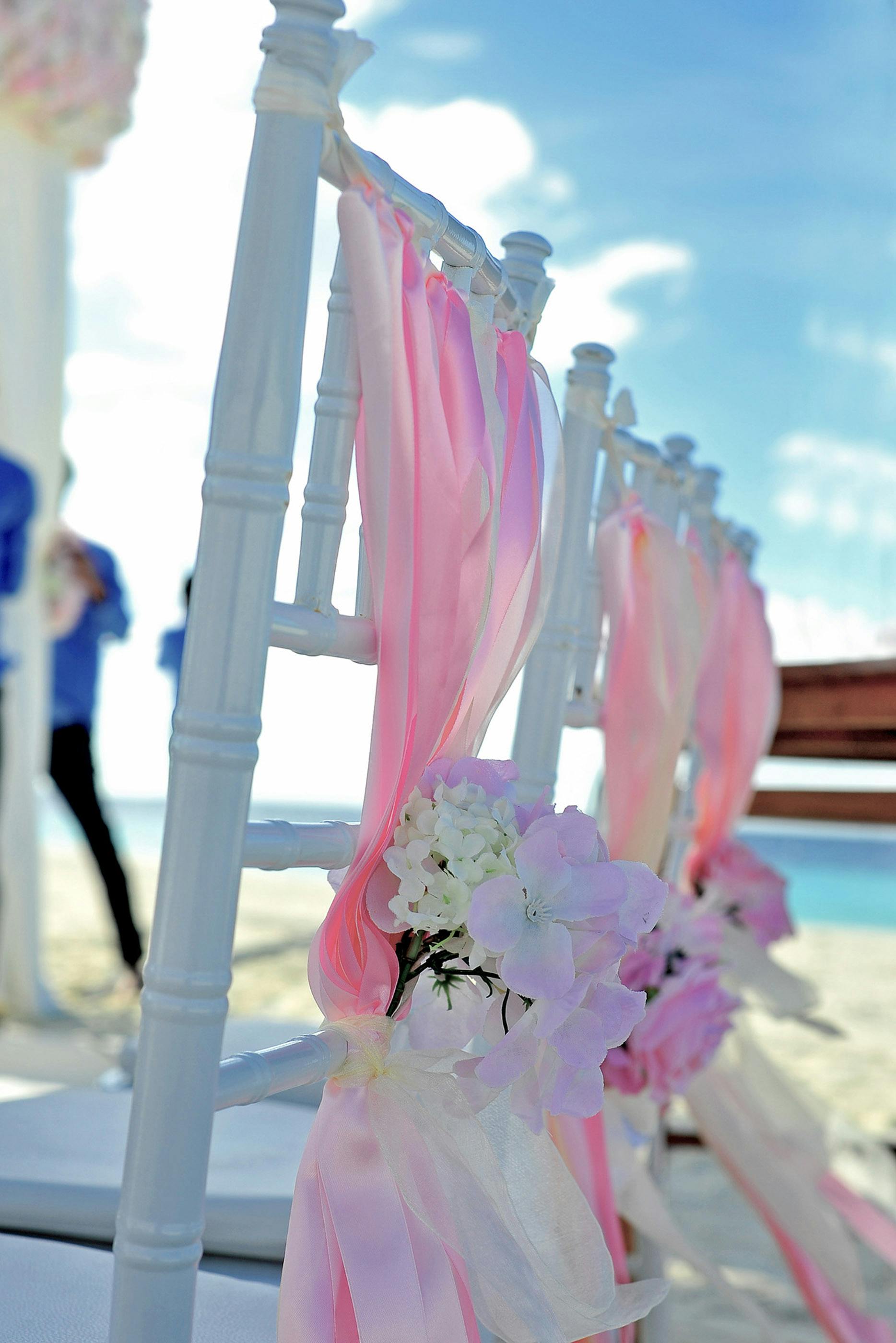 White chairs with pink ribbons on a serene Maldivian beach wedding setup.