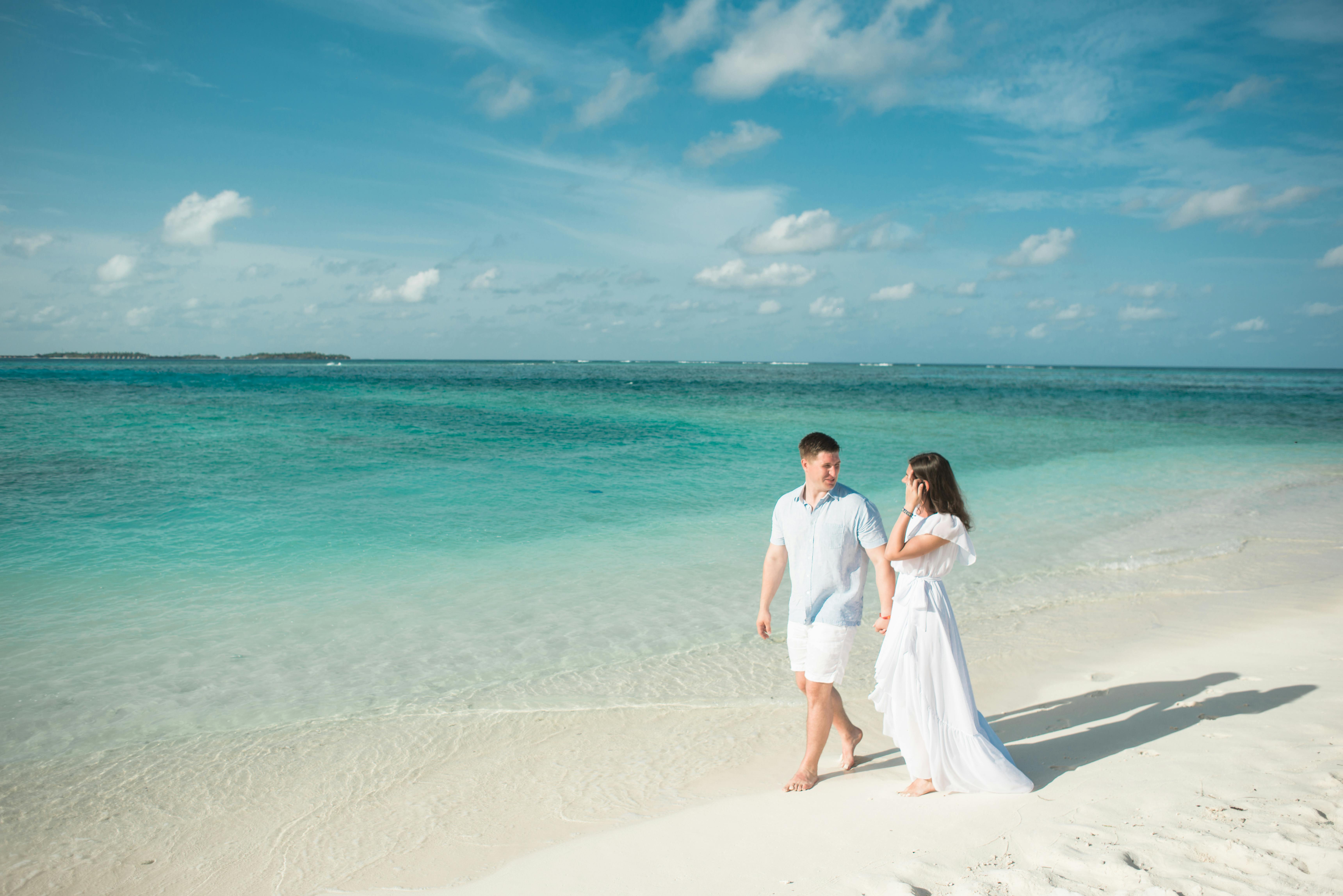 Couple walking hand in hand on a tropical beach, enjoying a romantic moment under a bright sky.